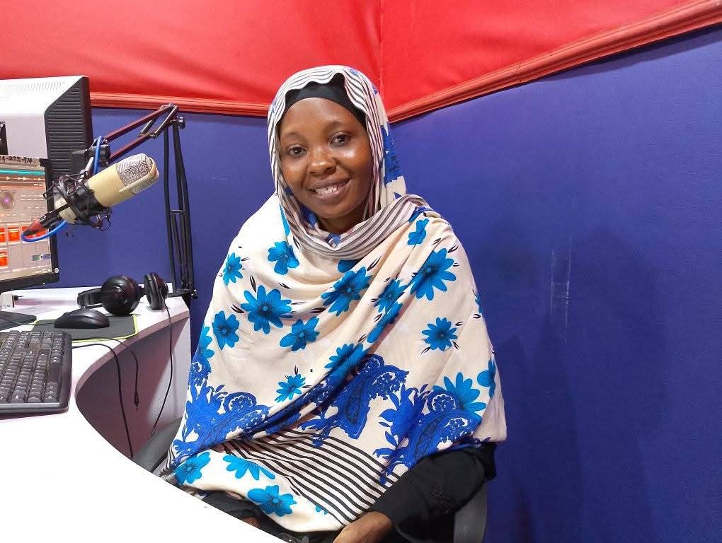 Presenter smiling beside the studio microphone at JAC FM